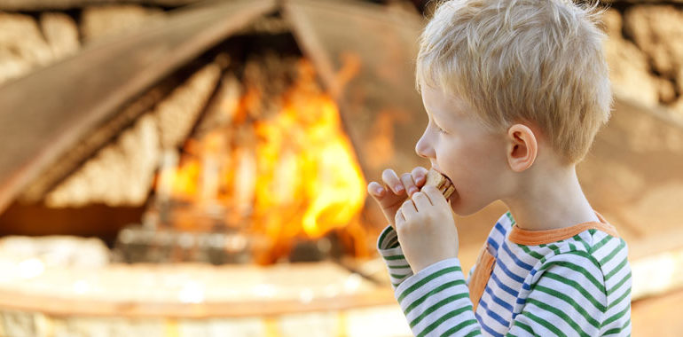 Un enfant mangeant un sandwich s'more près d'un feu de camp