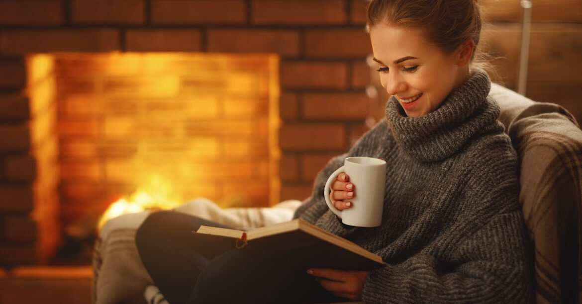 A woman enjoy a warm beverage by the fireplace reading a book