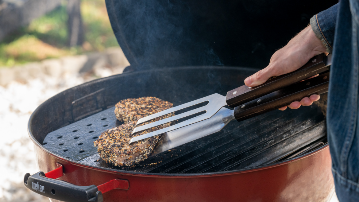 Someone is turning a piece of meat with tong on a bbq