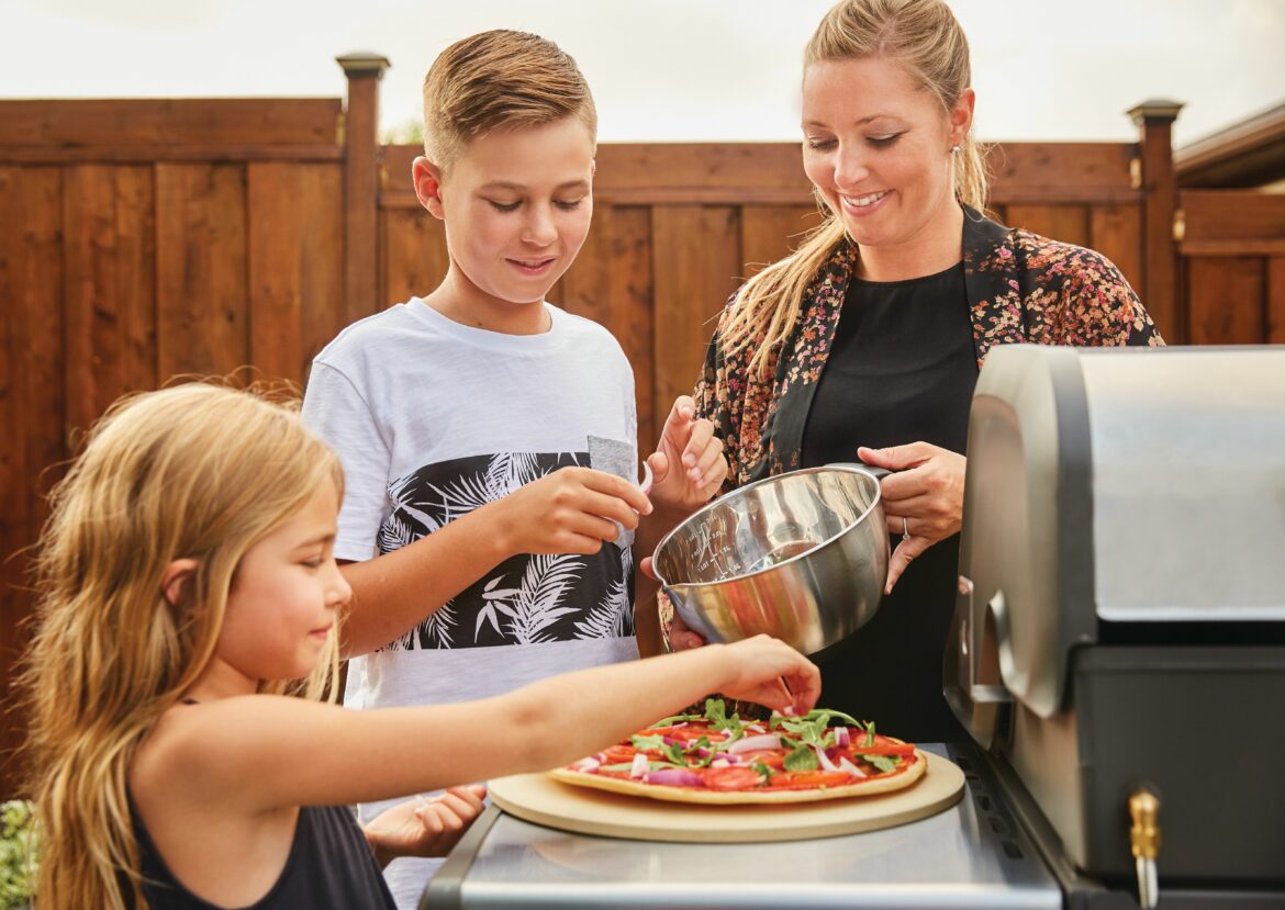 2 children and their mother are making a pizza on a pizza stone 