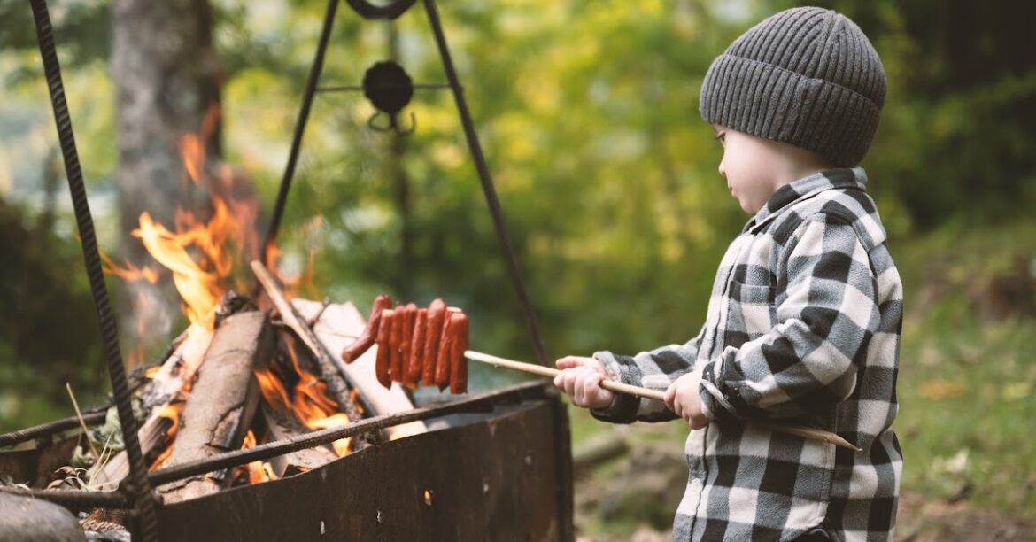 A little boy is cooking sausages on an open fire