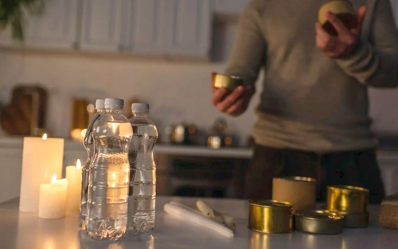 Bottled water, canned food and lit candles on a kitchen counter, ready for a power outage at home